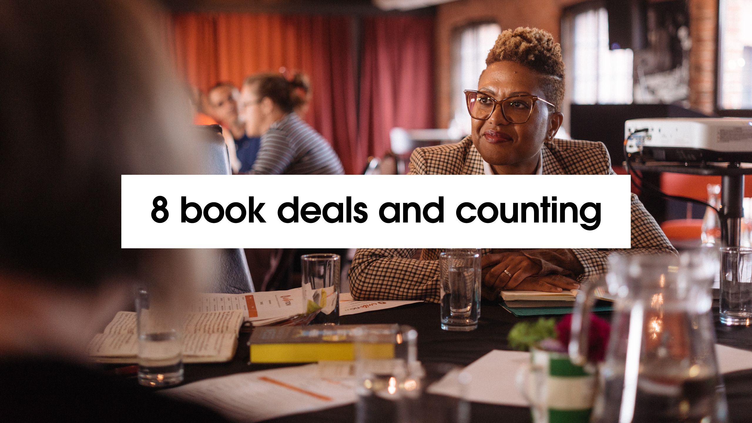 '8 book deals and counting' with background image of author Sara Collins at Liverpool WriteNow event.