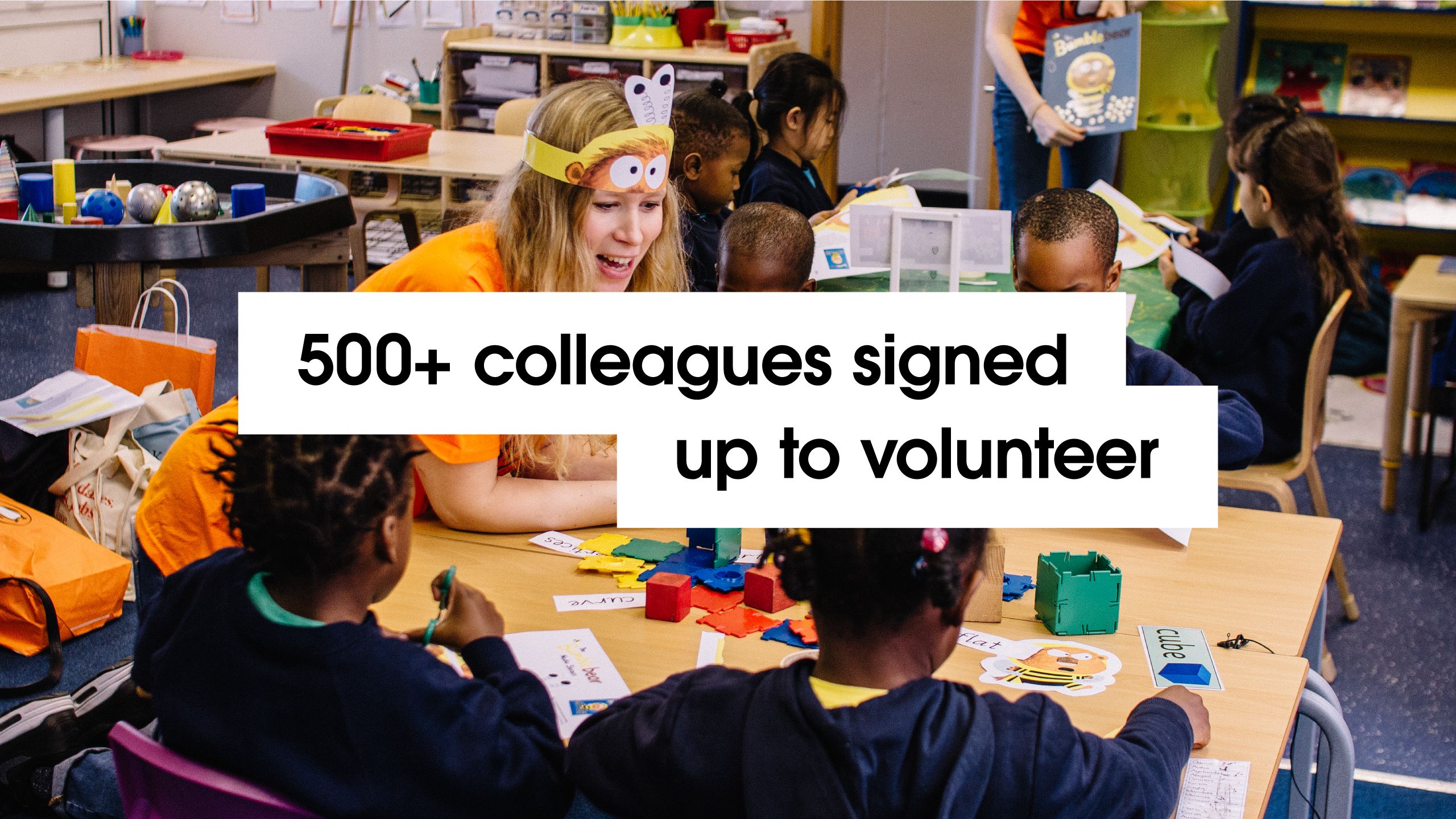 '500+ colleagues signed up to volunteer' - with background image of Penguin Random House staff interacting with primary school children as part of World Book Day.