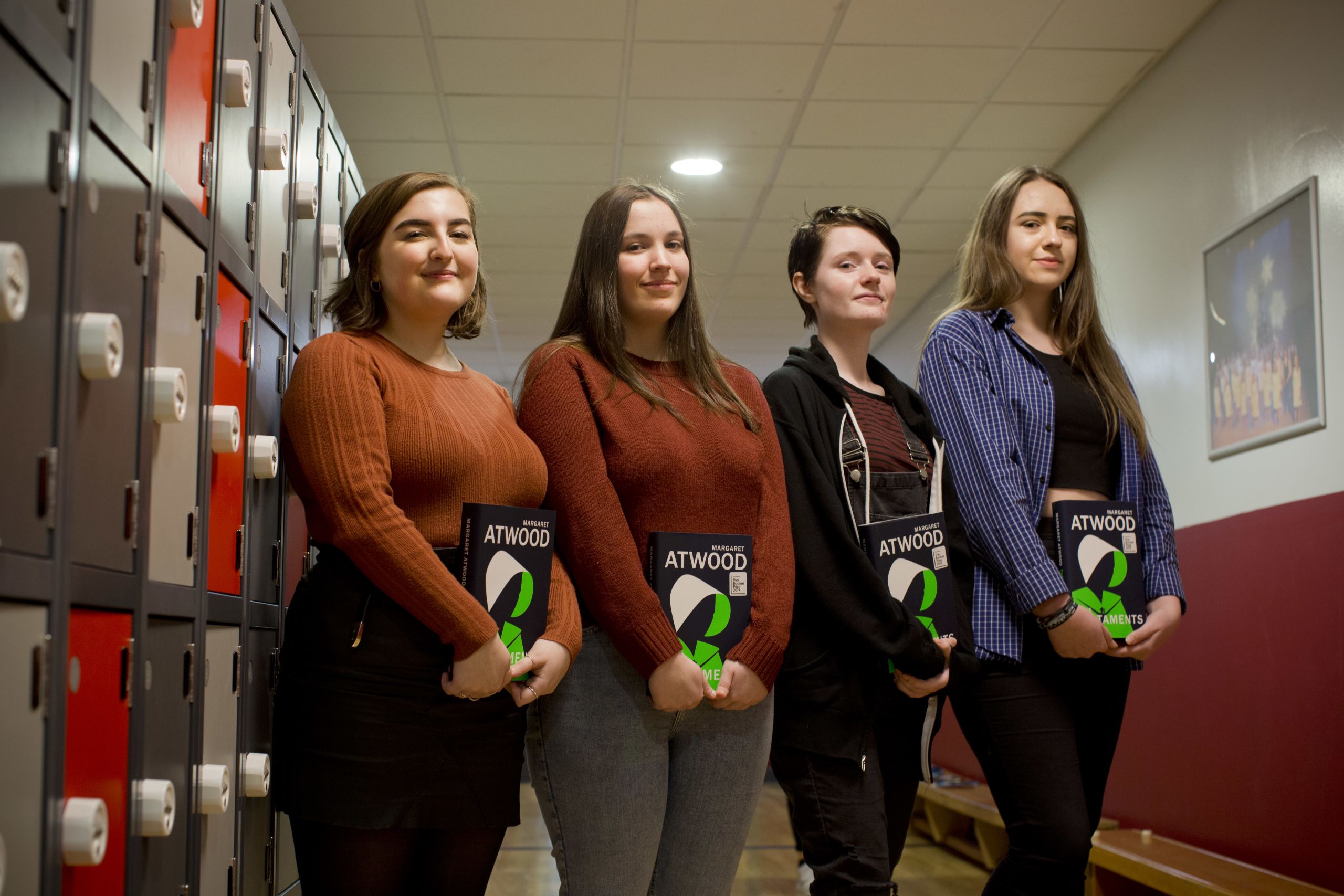 Four teenage girls holding copies of The Testaments in front of lockers at Pendleton Secondary School.